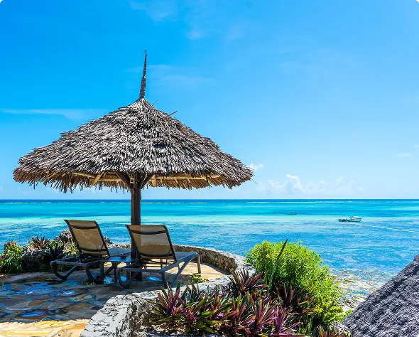 Beach loungers under a thatched umbrella overlooking the ocean, featured in the Zanzibar beach holiday itinerary